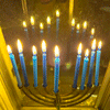 Rainbow Squared year 5, Piece Forty-Three: 19. Yellow Blue. A photo animation of a chanukiah with nine lit blue candles burning in a window with a reflected flame, with the candles layering and dancing on top of each other.
